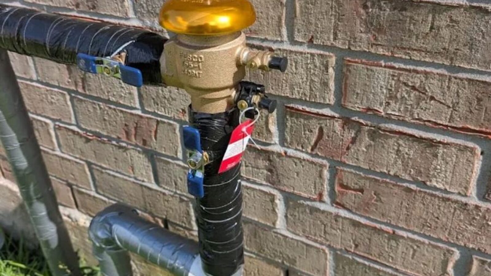 Brass backflow prevention assembly installed on an irrigation line beside a house