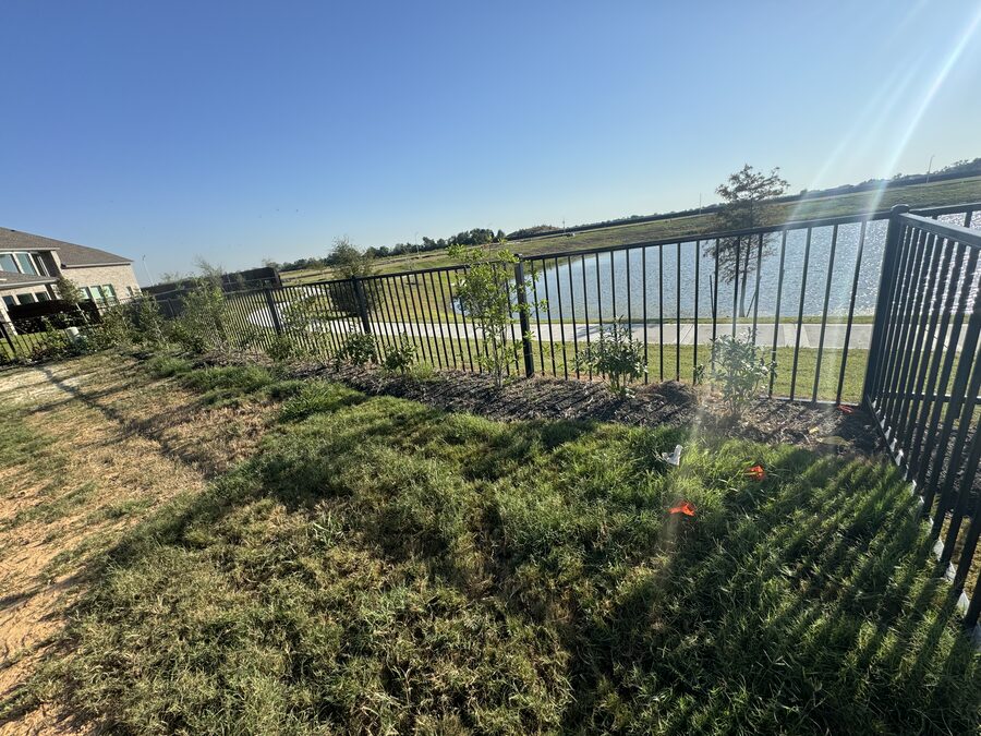 New flower bed and young plantings installed along a backyard fence overlooking the lake